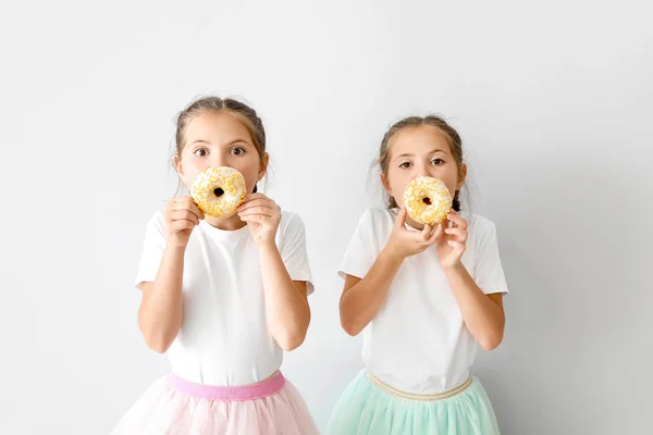 Ritratto di belle ragazze gemelle con gustose ciambelle su sfondo chiaro — Foto Stock