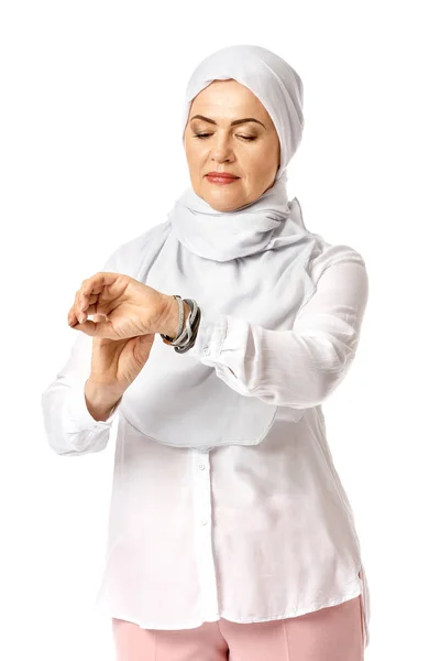 Beautiful mature Muslim woman looking on her wrist watch on white background — Stock Photo, Image