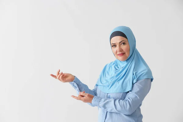 Schöne reife muslimische Frau zeigt etwas auf hellem Hintergrund — Stockfoto