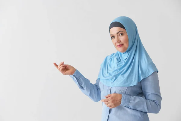 Mulher muçulmana madura bonita mostrando algo no fundo de luz — Fotografia de Stock