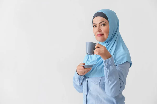 Schöne reife muslimische Frau mit einer Tasse Kaffee auf hellem Hintergrund — Stockfoto