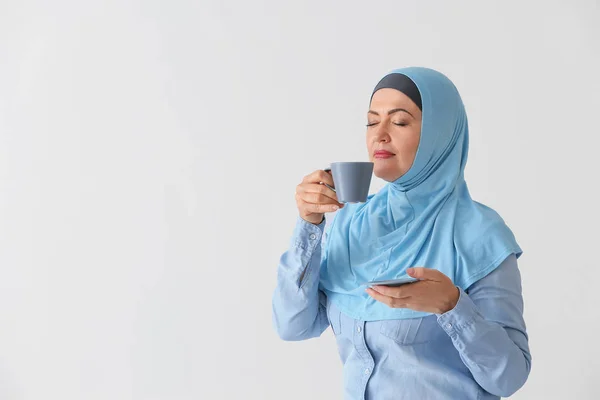 Beautiful mature Muslim woman with cup of coffee on light background — Stock Photo, Image