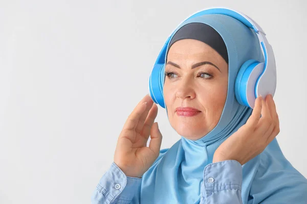 Beautiful mature Muslim woman listening to music on light background — Stock Photo, Image