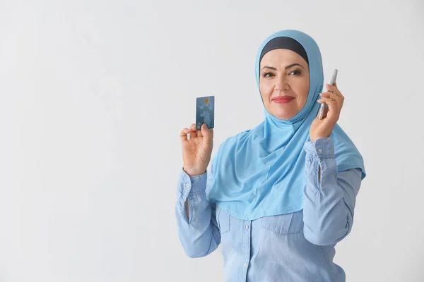 Mulher muçulmana madura bonita com cartão de crédito e telefone celular no fundo claro — Fotografia de Stock