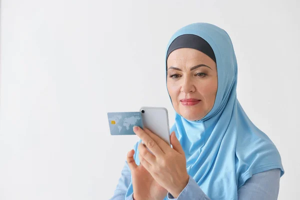 Hermosa mujer musulmana madura con tarjeta de crédito y teléfono móvil sobre fondo claro —  Fotos de Stock