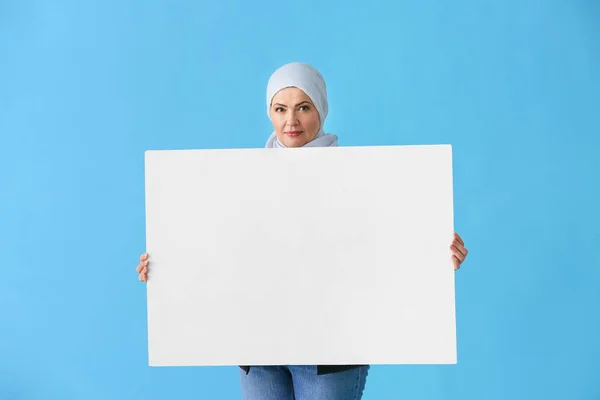 Beautiful mature Muslim woman with blank poster on color background — Stock Photo, Image