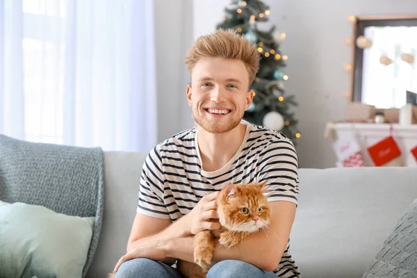 Young man with cute cat at home on Christmas eve