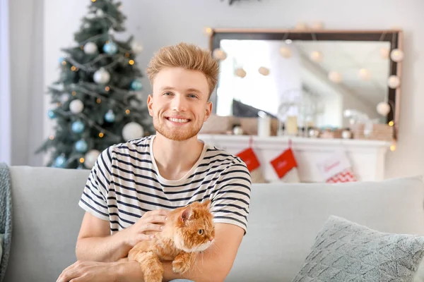 Young man with cute cat at home on Christmas eve