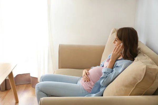 Beautiful pregnant woman talking by phone while sitting on sofa at home — Stock Photo, Image