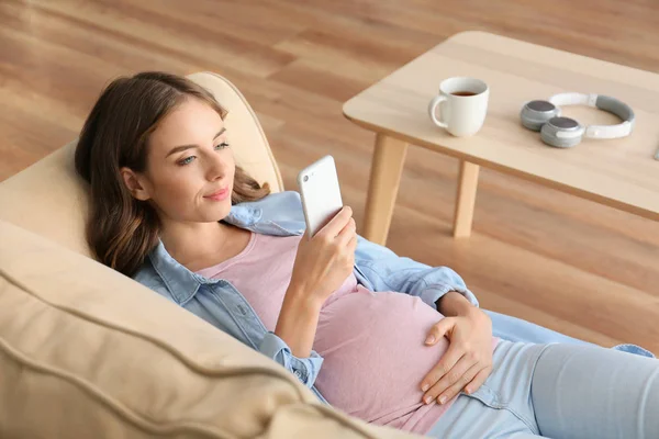 Beautiful pregnant woman with mobile phone lying on sofa at home