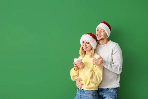 Feliz pareja en los sombreros de Santa beber chocolate caliente en el fondo de color — Foto de Stock