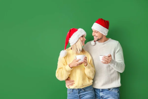 Feliz casal em Santa chapéus beber chocolate quente no fundo de cor — Fotografia de Stock