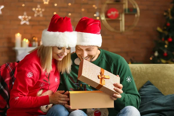 Happy couple in Santa hats and with Christmas gift at home — Stock Photo, Image