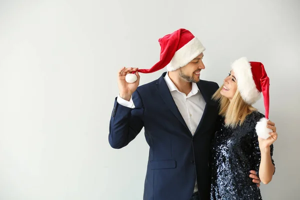 Happy couple in Santa hats on light background — Stock Photo, Image