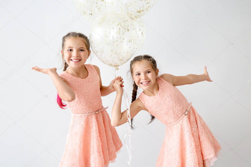 Portrait of happy twin girls with air balloons on light background