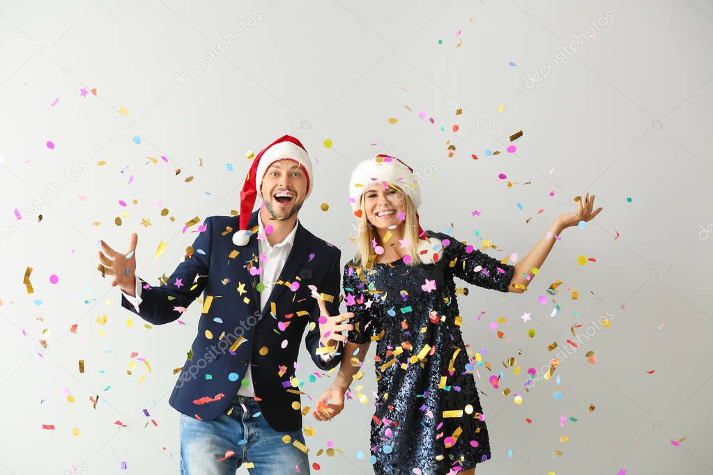 Happy couple in Santa hats and falling confetti on light background