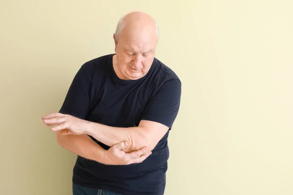 Senior man suffering from pain in elbow on light background — Stock Photo, Image