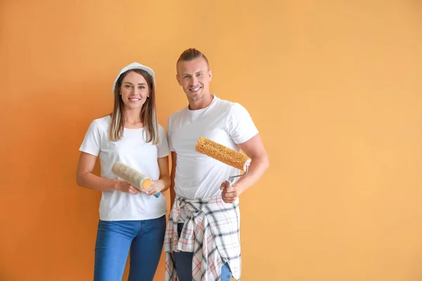 Feliz pareja joven con rodillos de pintura sobre fondo de color — Foto de Stock