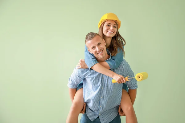 Feliz pareja joven con rodillo de pintura sobre fondo de color — Foto de Stock