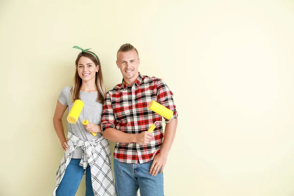 Feliz pareja joven con rodillos de pintura cerca de la pared de color — Foto de Stock