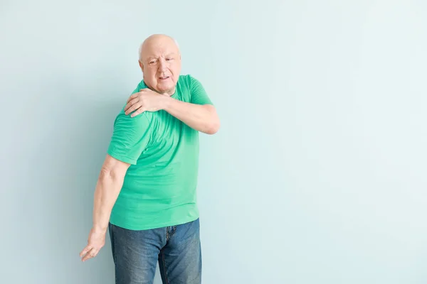 Senior leidet an Schulterschmerzen vor hellem Hintergrund — Stockfoto