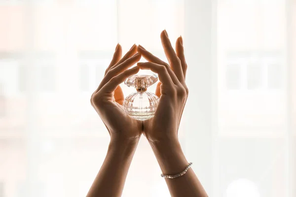 Handen van mooie jonge vrouw met fles parfum in de buurt van venster — Stockfoto
