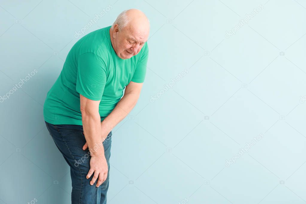 Senior man suffering from pain in knee on light background