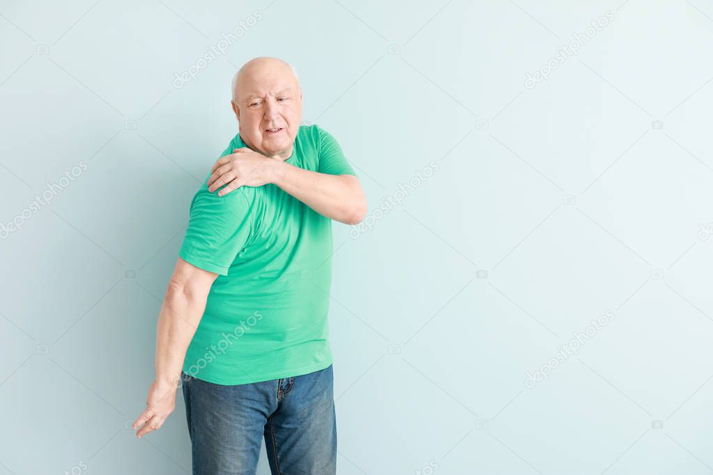 Senior man suffering from pain in shoulder on light background
