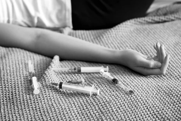 Photo en noir et blanc d'une jeune femme inconsciente avec des seringues couchées sur le lit. Concept de suicide — Photo