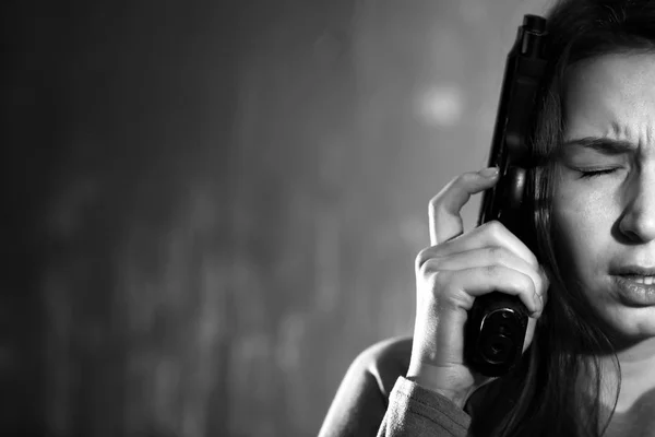 Black and white photo of young depressed woman with gun thinking about suicide on dark background — Stock Photo, Image