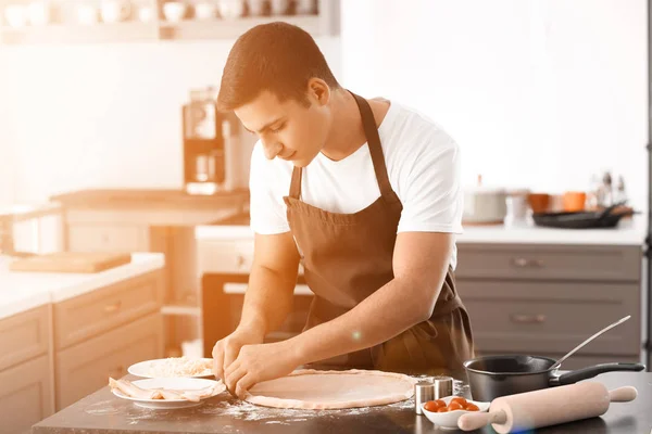 Mladý muž připravuje chutné pizzy v kuchyni — Stock fotografie