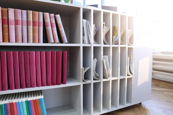 Many books, magazines and newspapers on shelves in modern library