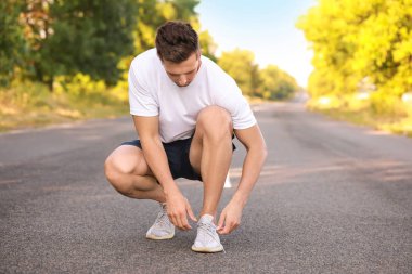 Spor ayakkabı bağcıklarını bağlayan genç bir adam.