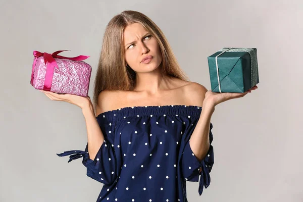 Thoughtful young woman with gifts on grey background — Stock Photo, Image