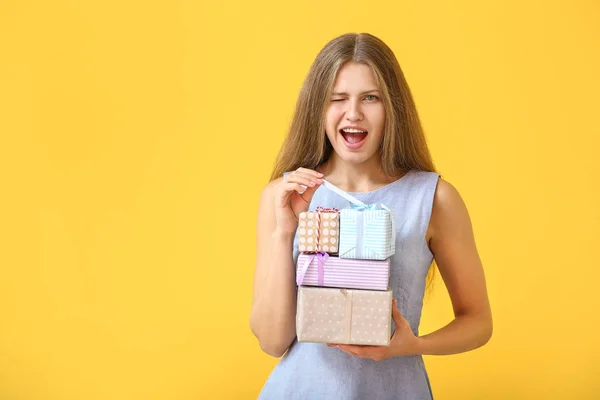Schöne junge Frau mit Geschenken auf farbigem Hintergrund — Stockfoto