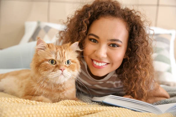 Young African-American woman with cute cat reading book at home — Stock Photo, Image