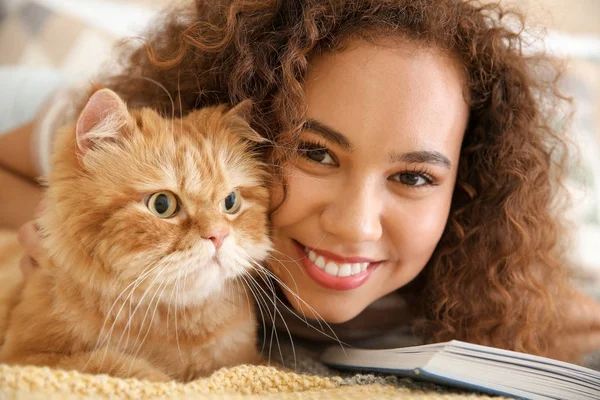 Young African-American woman with cute cat reading book at home — Stock Photo, Image