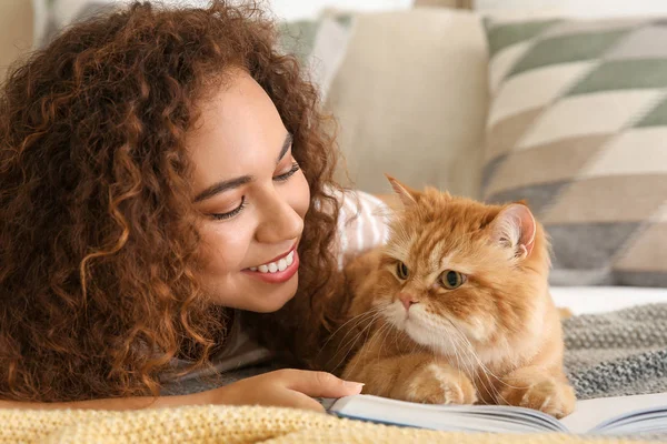 Jovem afro-americano mulher com bonito gato leitura livro em casa — Fotografia de Stock