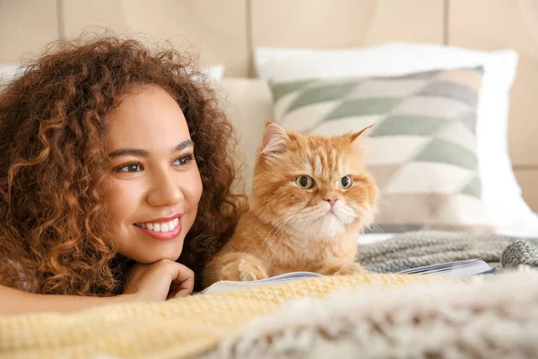 Young African-American woman with cute cat reading book at home — Stock Photo, Image