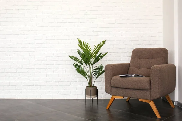 Elegante sillón con planta tropical cerca de la pared de ladrillo blanco en la habitación —  Fotos de Stock