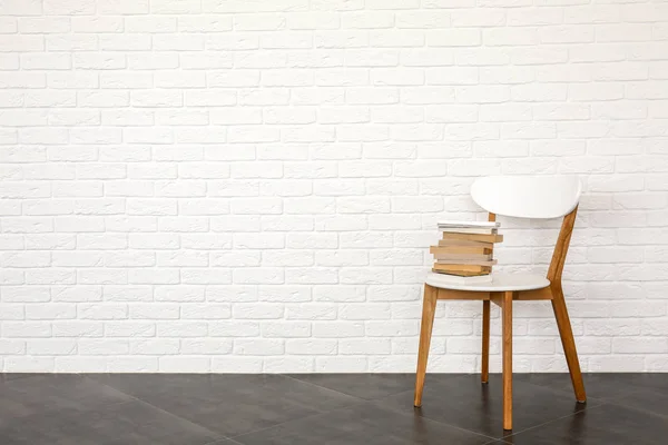 Stapel boeken op stoel in de buurt van witte bakstenen muur — Stockfoto