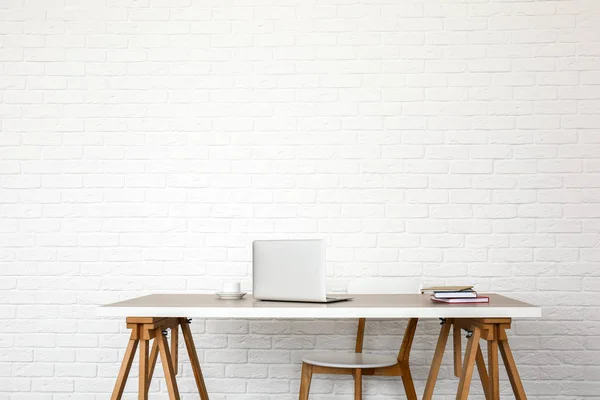 Mesa con portátil moderno y silla cerca de la pared de ladrillo blanco —  Fotos de Stock