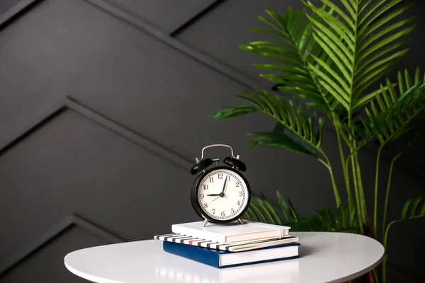 Relógio despertador e cadernos na mesa contra a parede escura — Fotografia de Stock