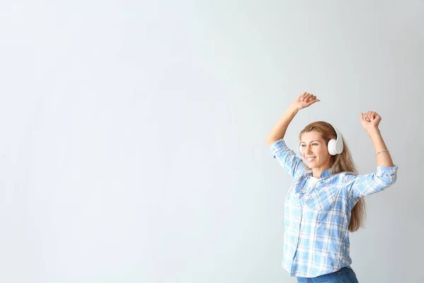 Dancing young woman with headphones on light background — Stock Photo, Image