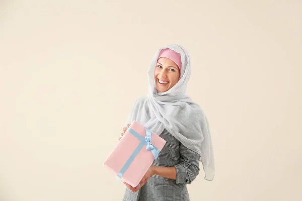 Beautiful young Muslim woman with gift on light background — Stock Photo, Image