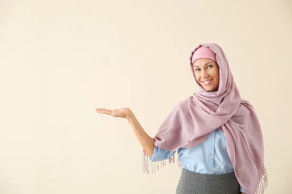 Beautiful young Muslim woman showing something on light background — Stock Photo, Image