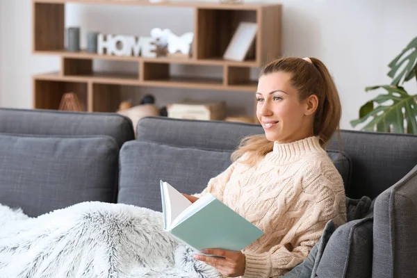 Beautiful young woman reading book at home — Stock Photo, Image