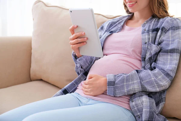 집에서 소파에 앉아 태블릿 컴퓨터와 아름다운 임신 한 여자 — 스톡 사진
