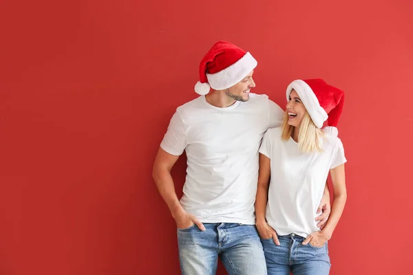Happy couple in Santa hats on color background — Stock Photo, Image