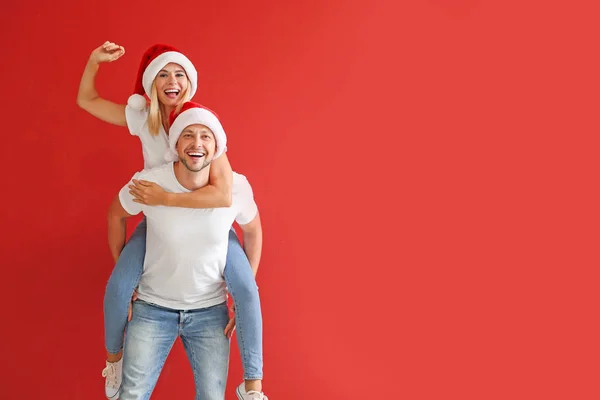 Happy couple in Santa hats on color background — Stock Photo, Image